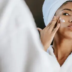 Frau mit Handtuch auf dem Kopf trägt Creme auf, die Glykolsäure und Niacinamid enthält.