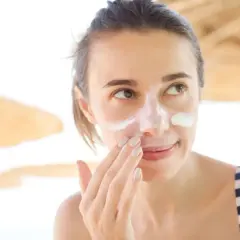 Frau trägt Sonnencreme auf ihr Gesicht auf, um Sonnenbrand zu vermeiden.