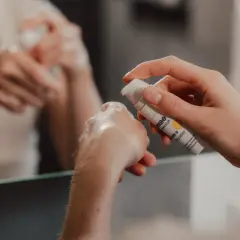 Eine Hand hält eine Flasche mit Vitamin C Booster. Ein Tropfen Serum landet auf der anderen Hand, bereit für die abendliche Hautpflege.