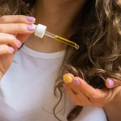 Hände mit lila und gelbem Nagellack tragen Rizinusöl (castor oil) auf lockiges Haar auf.