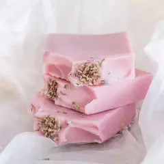 Zarte rosa Seifenstücke mit Lavendelblüten, inspiriert von Quillaja Saponaria, liegen auf weißem Papier.