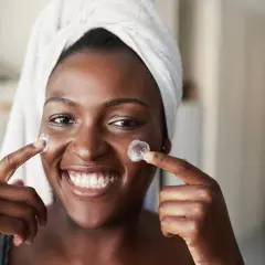 Lächelnde Frau mit Handtuch auf dem Kopf trägt Creme auf. Frage: Retinol wie oft?