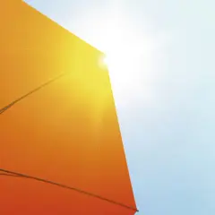 Ein orangefarbener Sonnenschirm schützt vor der Sonne. Seine Struktur ist sichtbar, während Sonnenstrahlen durchscheinen. Diethylhexyl Butamido Triazone schützt die Haut.