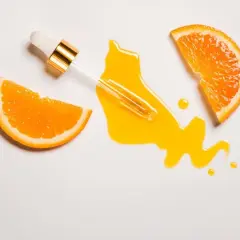 Ein Pipettenfläschchen tropft ein leuchtendes Serum neben Orangenscheiben. Vitamin C für das Gesicht, das für strahlende Haut sorgt.