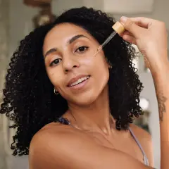 Frauen mit lockigem Haar tragen ein Serum mit Peptiden auf, um ihre Haut mit Feuchtigkeit zu versorgen.