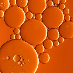 Orangefarbene Bläschen, wie von Butylmethoxydibenzoylmethan, schweben auf einem warmen, orangen Hintergrund.