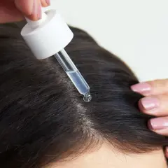 Eine Pipette mit Serum tropft auf die Kopfhaut, um das Haarwachstum mit Retinol zu fördern.