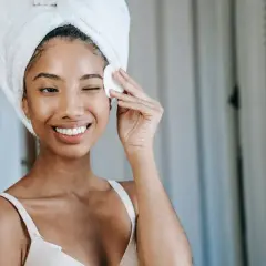Lächelnde Frau mit Handtuch auf dem Kopf entfernt mit Wattepad Make-up.