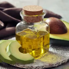 Flasche mit goldenem Persea gratissima oil neben frischen Avocadoscheiben und einer halben Avocado.