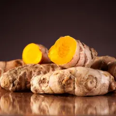 Ein Haufen frischer Kurkumawurzeln, eine davon aufgeschnitten, enthüllt ihr leuchtend orangefarbenes Inneres und die wertvollen Kurkuma Inhaltsstoffe.