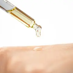 Tropfen eines goldenen Öls fallen aus einer Pipette auf die Haut. Glycerin ist ein Feuchtigkeitsspender, der die Haut geschmeidig macht.