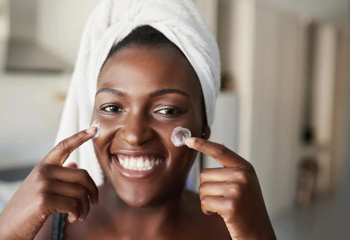 Lächelnde Frau mit Handtuch auf dem Kopf trägt Creme auf. Frage: Retinol wie oft?