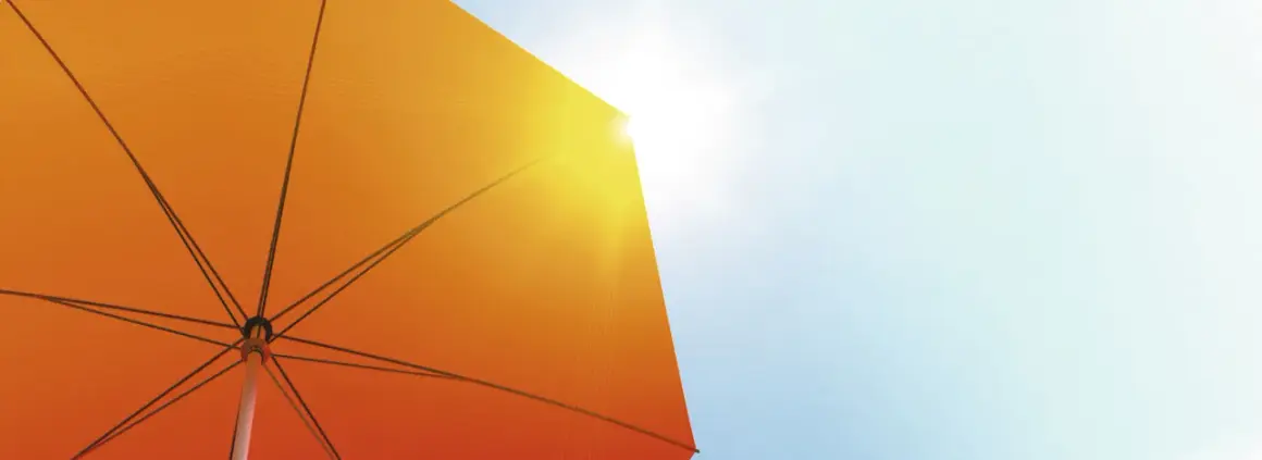 Ein orangefarbener Sonnenschirm schützt vor der Sonne. Seine Struktur ist sichtbar, während Sonnenstrahlen durchscheinen. Diethylhexyl Butamido Triazone schützt die Haut.