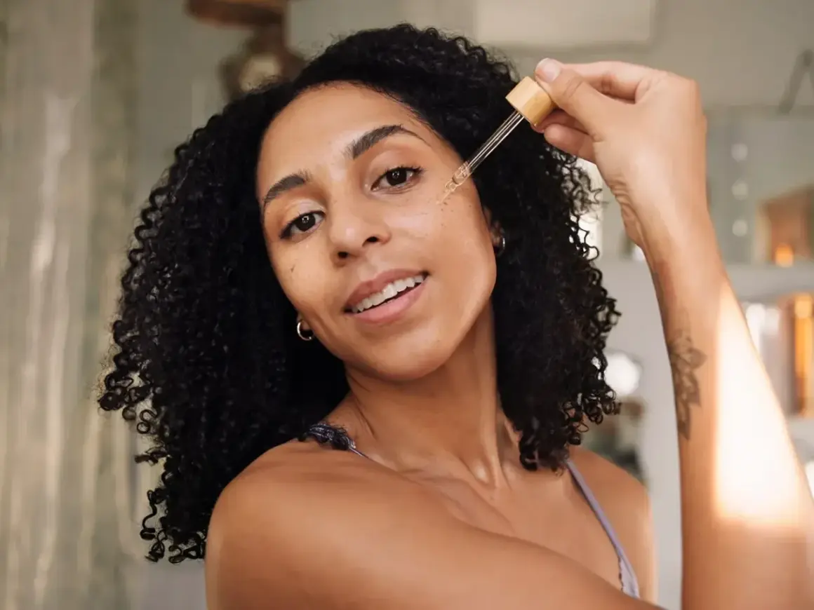 Frauen mit lockigem Haar tragen ein Serum mit Peptiden auf, um ihre Haut mit Feuchtigkeit zu versorgen.