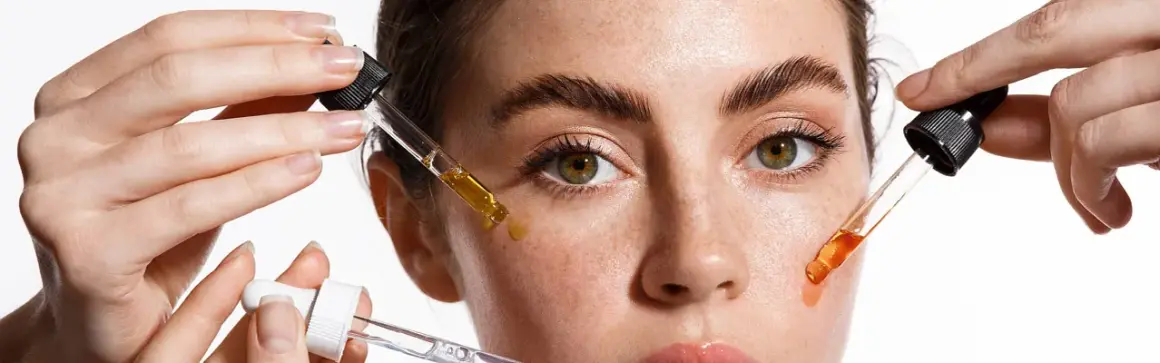 Hände tragen Pipetten mit Seren auf das Gesicht einer Frau auf. Diese Seren enthalten oft Peptide, die für die Hautpflege wichtig sind.