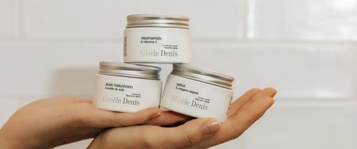 Hände halten drei Gisele Denis Cremetiegel: einer mit Niacinamid & Vitamin C, einer mit Hyaluronsäure & Sojaöl, und einer mit Retinol & pflanzlichem Kollagen.