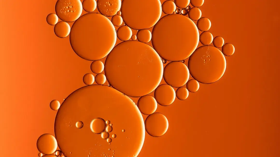 Orangefarbene Bläschen, wie von Butylmethoxydibenzoylmethan, schweben auf einem warmen, orangen Hintergrund.