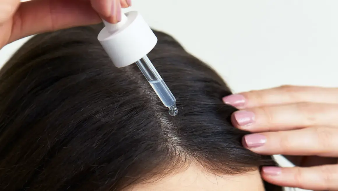 Eine Pipette mit Serum tropft auf die Kopfhaut, um das Haarwachstum mit Retinol zu fördern.