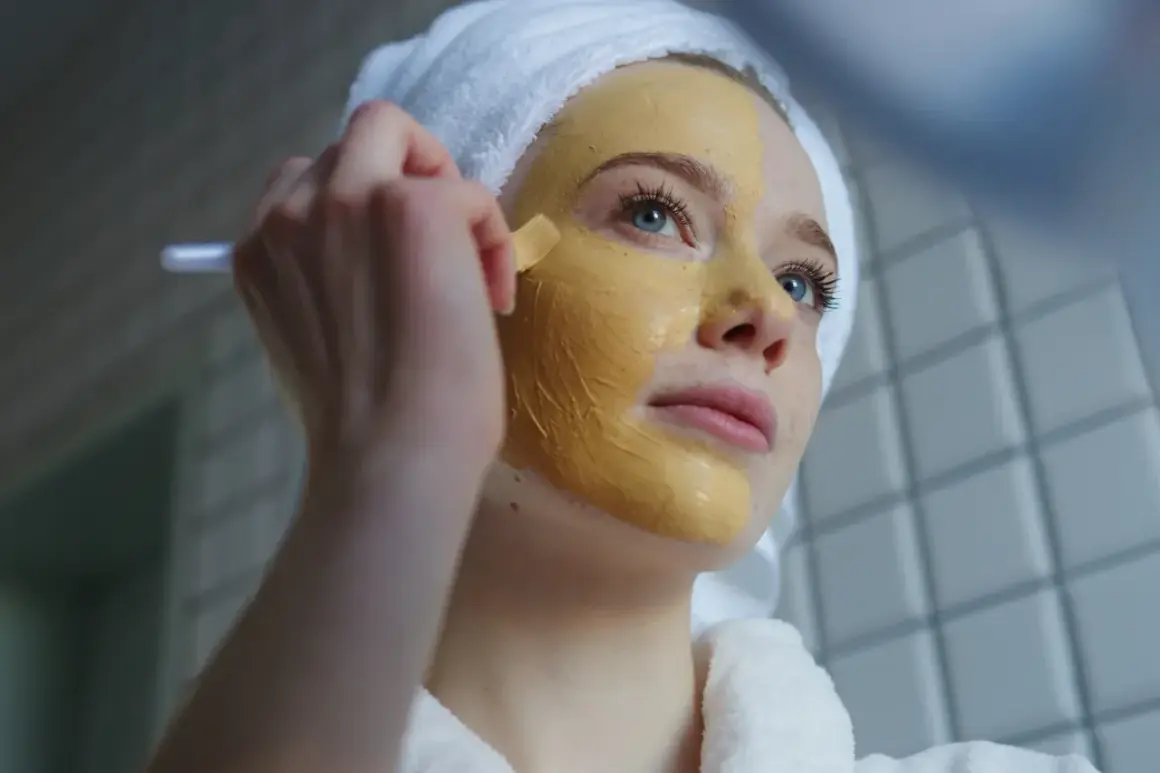 Junge Frau mit Handtuch auf dem Kopf trägt eine Kurkuma-Maske auf. Vorher-Nachher-Effekt für strahlende Haut.