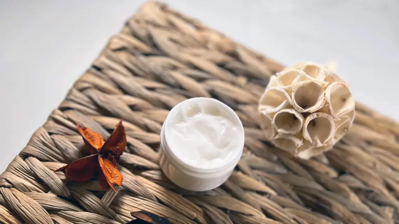 Ein weißer Tiegel mit cremiger Textur, ideal zum hyaluron creme selber machen. Daneben liegen getrocknete Naturmaterialien.