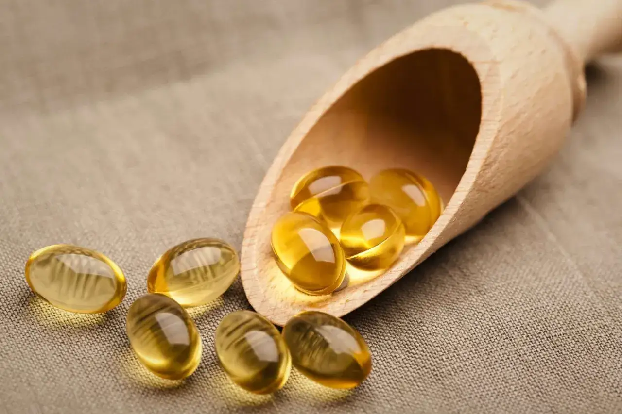 Gelatinekapseln mit Vitamin E in einem Holzschöpflöffel. Vorsicht bei der Einnahme, um Vitamin E Nebenwirkungen zu vermeiden.