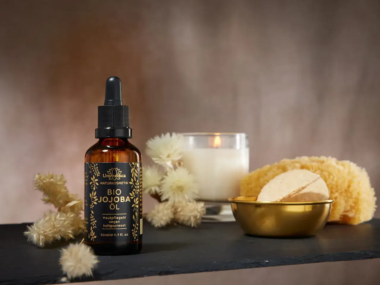 Eine Flasche BIO JOJOBA ÖL (Simmondsia Chinensis Seed Oil) steht neben einer Kerze und einem Schwamm.